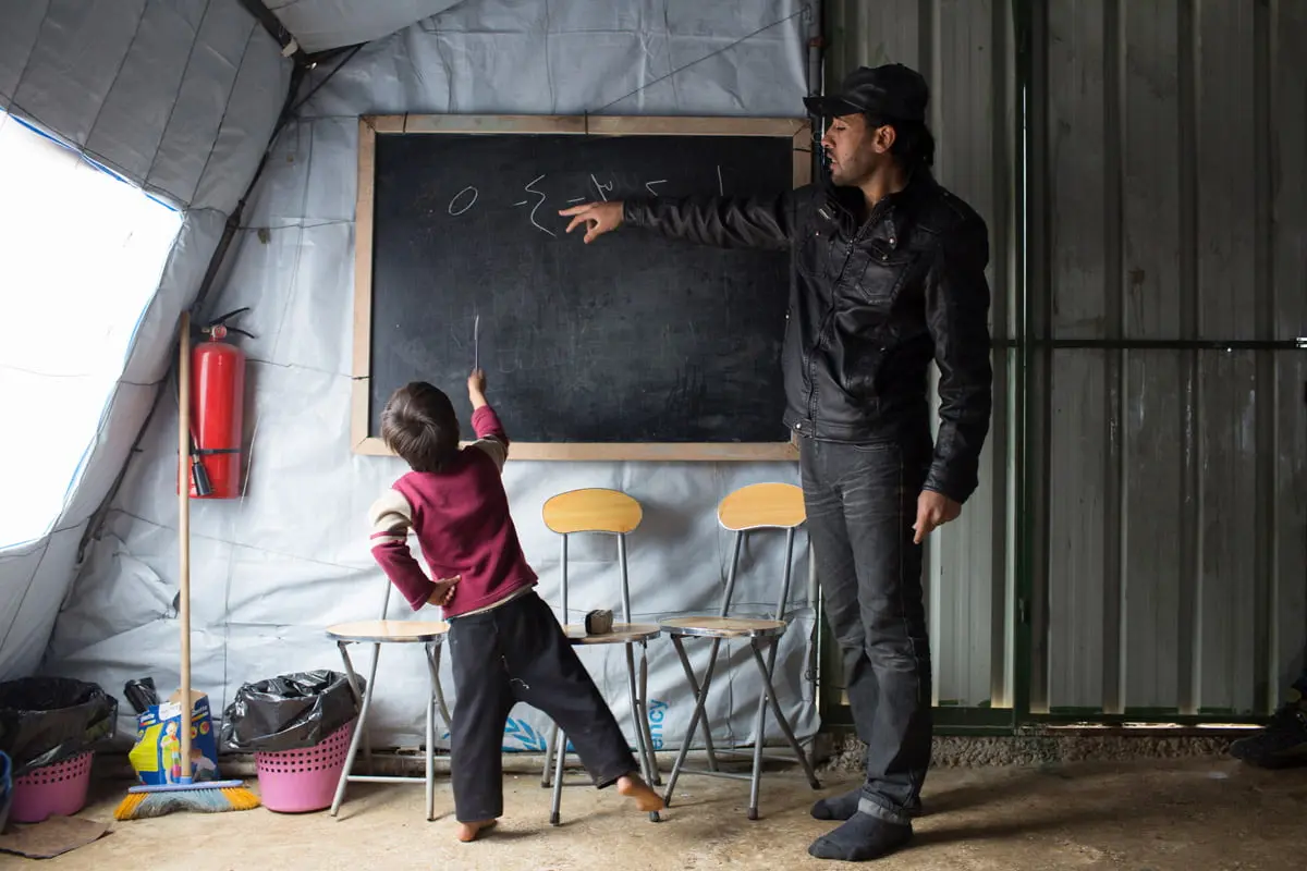 Syrian refugee Ayham* points at the number 4, written in Arabic, on the blackboard as a student counts numbers during a non-formal education program at an informal tented settlement in Mohamara, in Akkar, north of Lebanon. (Photo: Dalia Khamissy/Concern Worldwide)