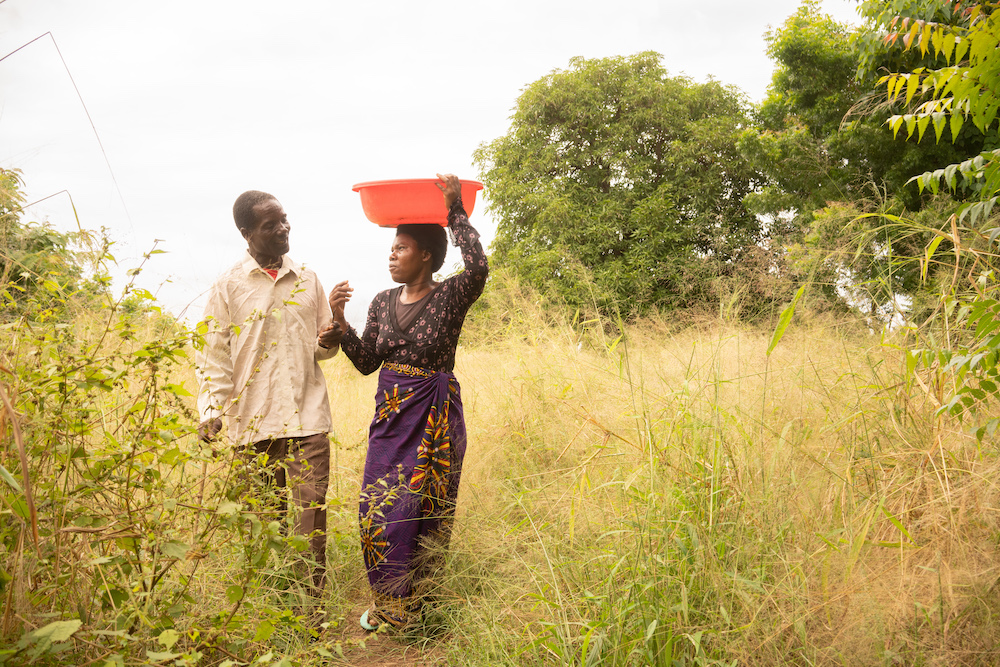 Stone and Rose walk to their garden to pick vegetables to sell at market. After finishing the Umodzi training, Stone takes an active part in Rose's farming business. (Photo: Chris Gagnon / Concern Worldwide)