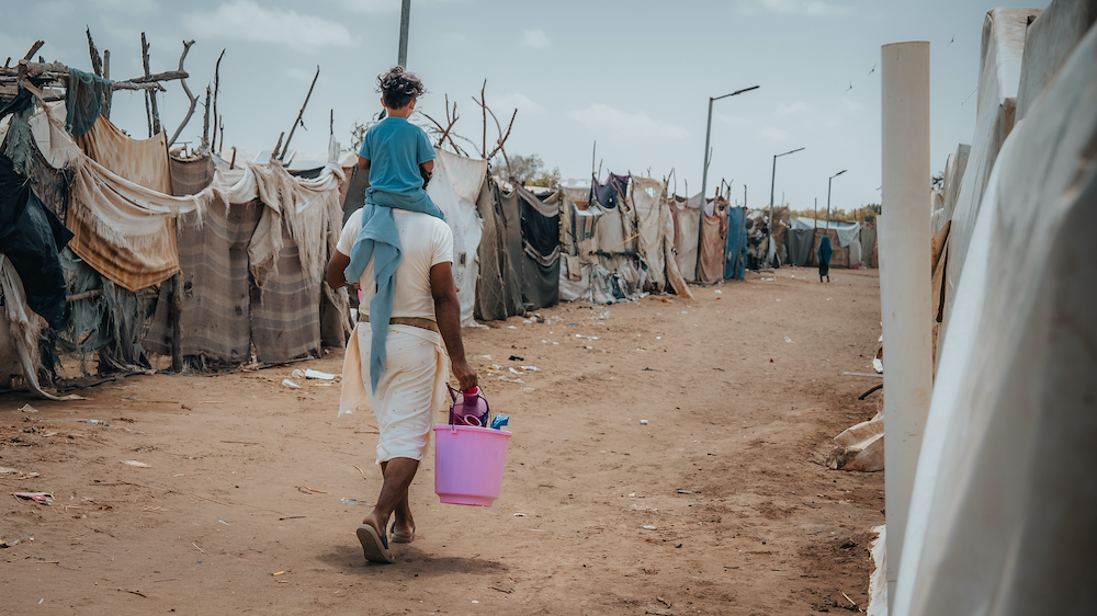 A child on his father’s back returning to their home after receiving a cholera/hygiene kit from Concern at Al-Salam IDP camp, Dar Saad district, Aden Governorate. (Photo: Ammar Khalaf/Concern Worldwide)