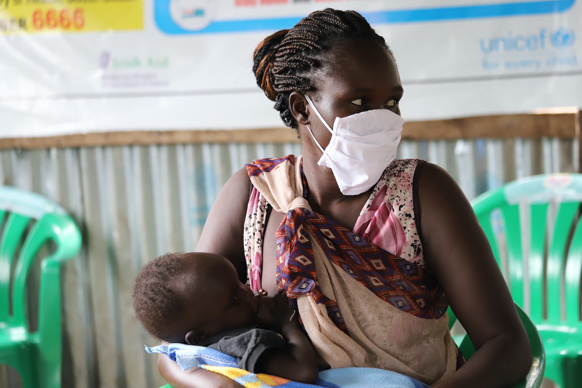 Nyaluit Khan and her 14-month-old child Chudier at a Concern Nutrition Centre in South Sudan to receive supplementary food to help increase their nutritional level. Nyaluit wears a mask while in the waiting areas of the center to help prevent the spread of COVID-19. (Photo: Samir Bol/ Concern Worldwide)