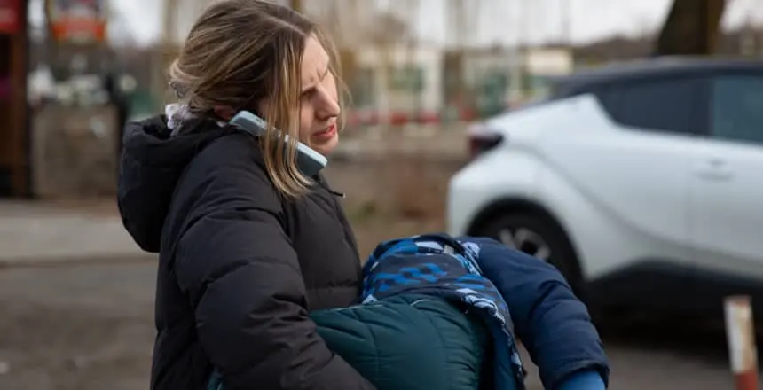 A mother talks on the phone while holding her young child and waiting on the Polish side of the border with Ukraine at Medyka.